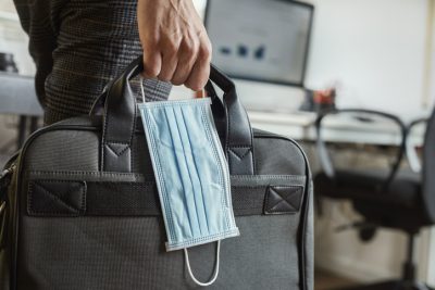 man holding a laptop bag and a face mask, prepared for the Winter economy plan